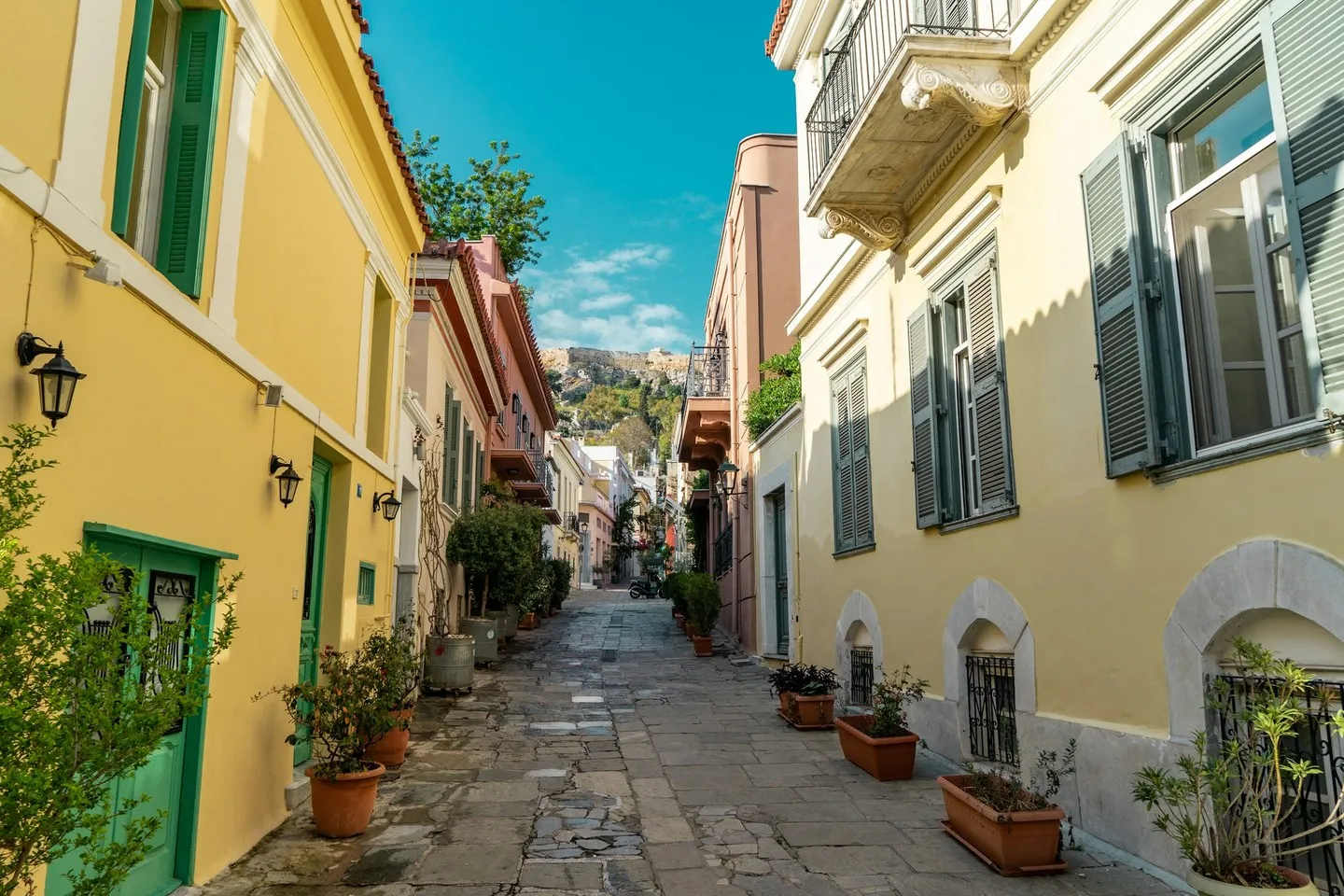Narrow stone-paved street in Plaka, Athens, with yellow houses, shutters and potted plants