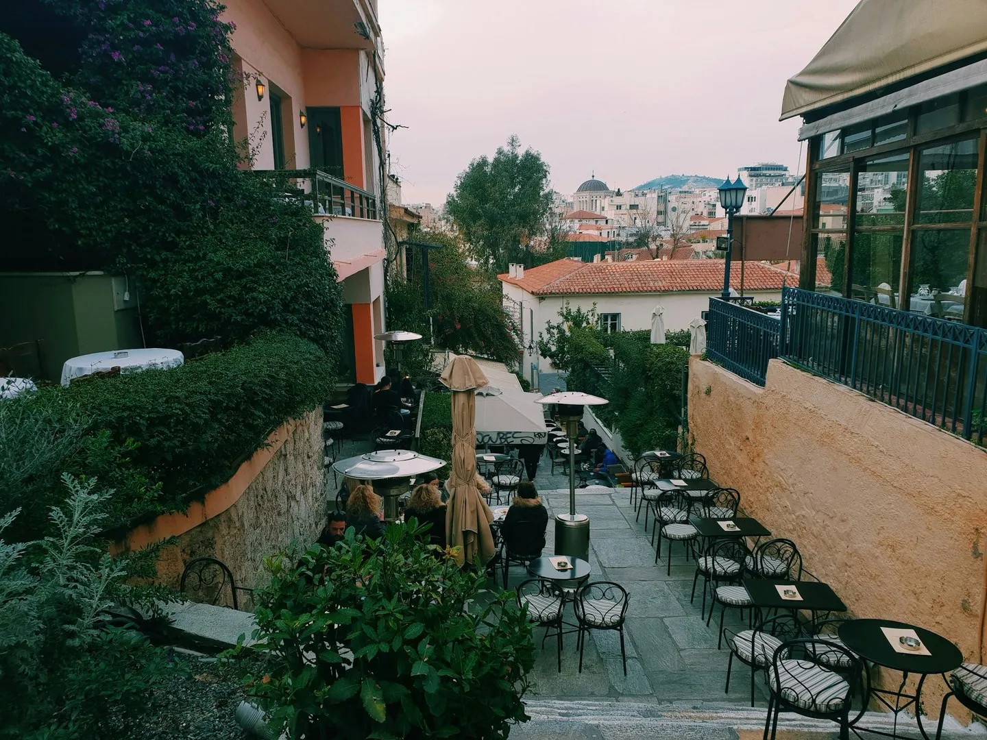 Terraced outdoor café patio with small tables and umbrellas in Plaka, Athens, rooftops beyond