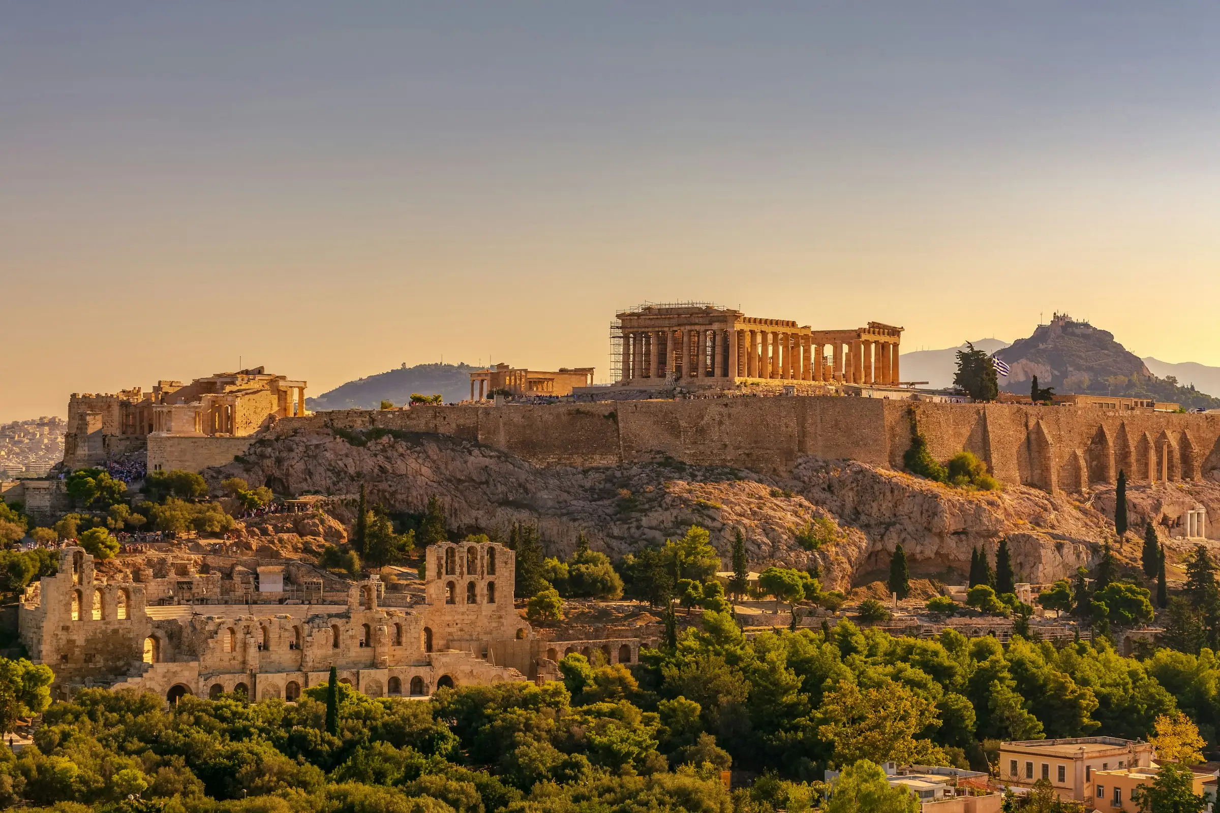 The Acropolis and Parthenon above pine trees in Athens at golden hour, a rocky hill behind