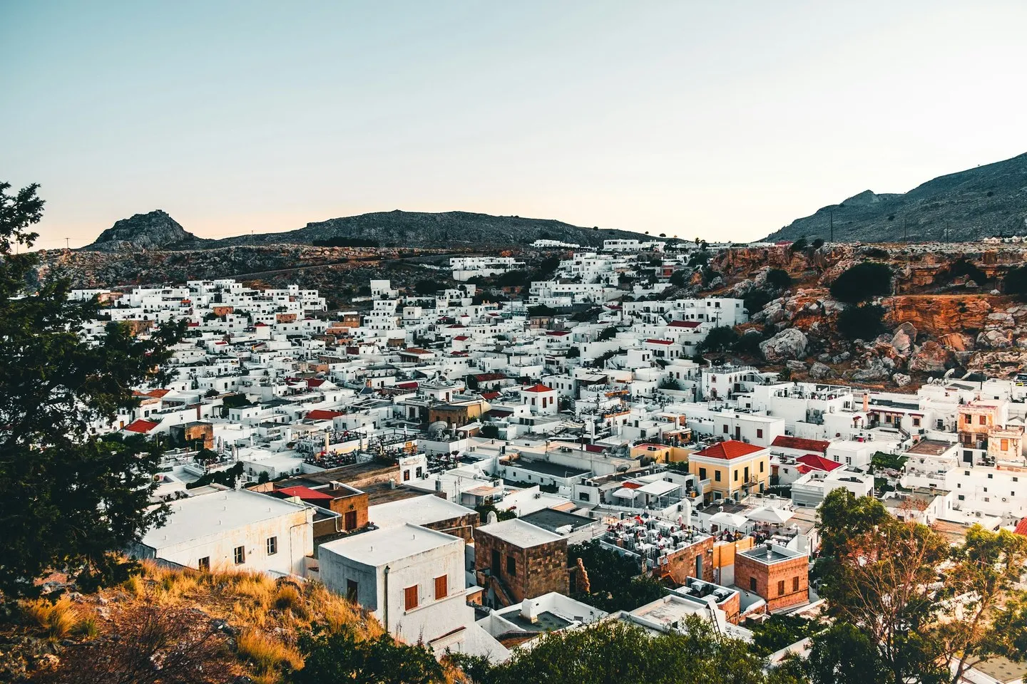 White houses and red roofs of a Rhodes hillside village below rocky mountains at dusk