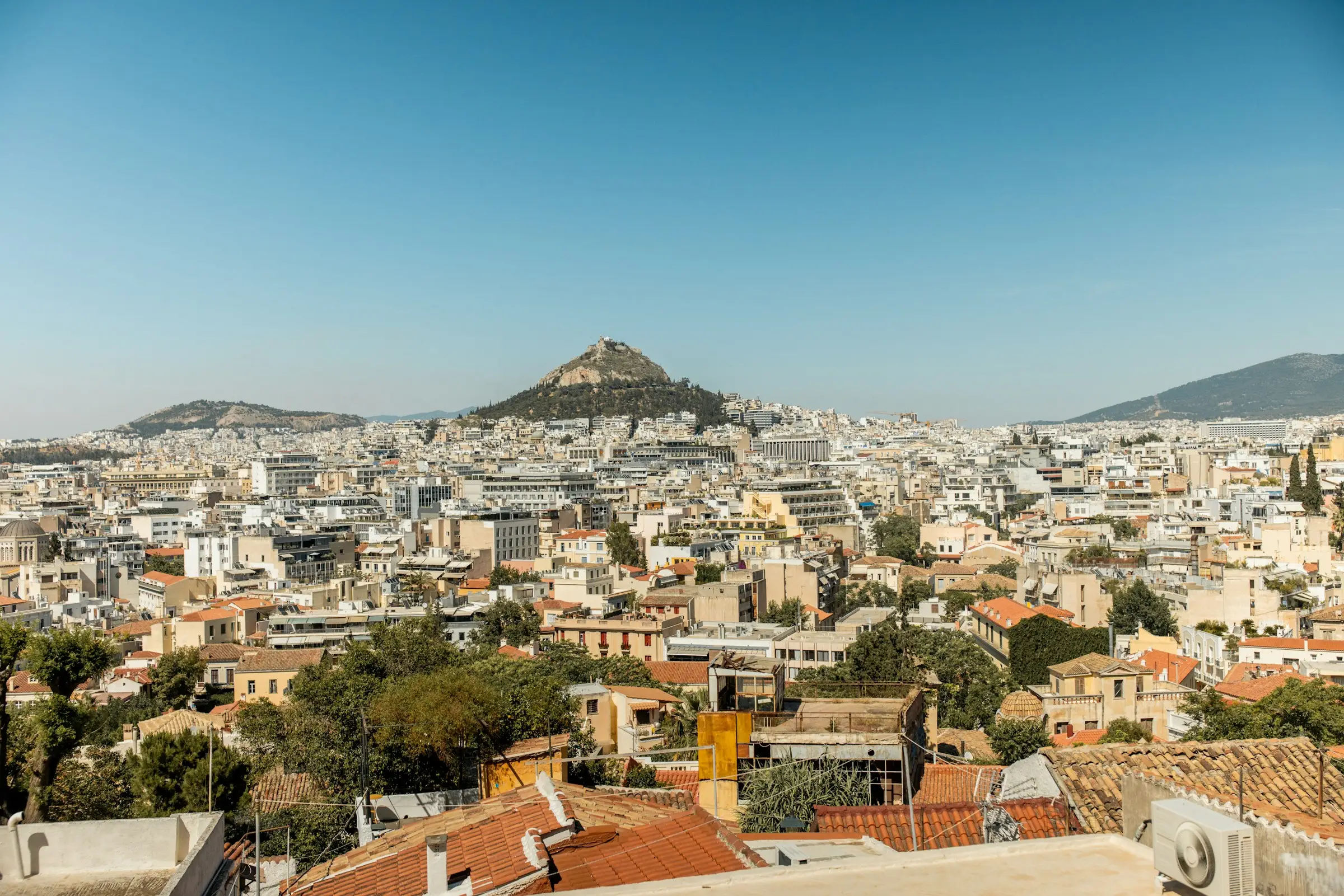 Athens rooftops and apartment blocks stretching towards Lycabettus Hill under a clear blue sky