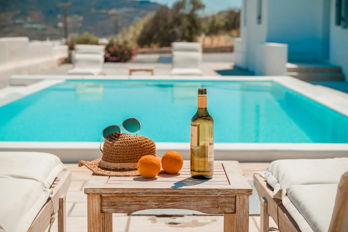 Mykonos pool terrace with a straw hat, sunglasses, oranges and a wine bottle on a table