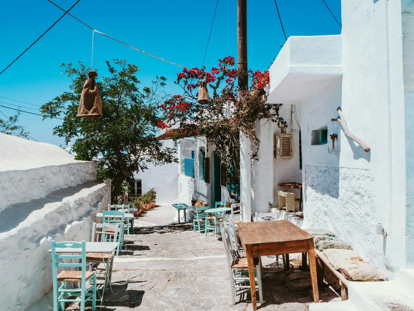 Whitewashed lane on Amorgos with wooden tables, pale blue chairs and red bougainvillea
