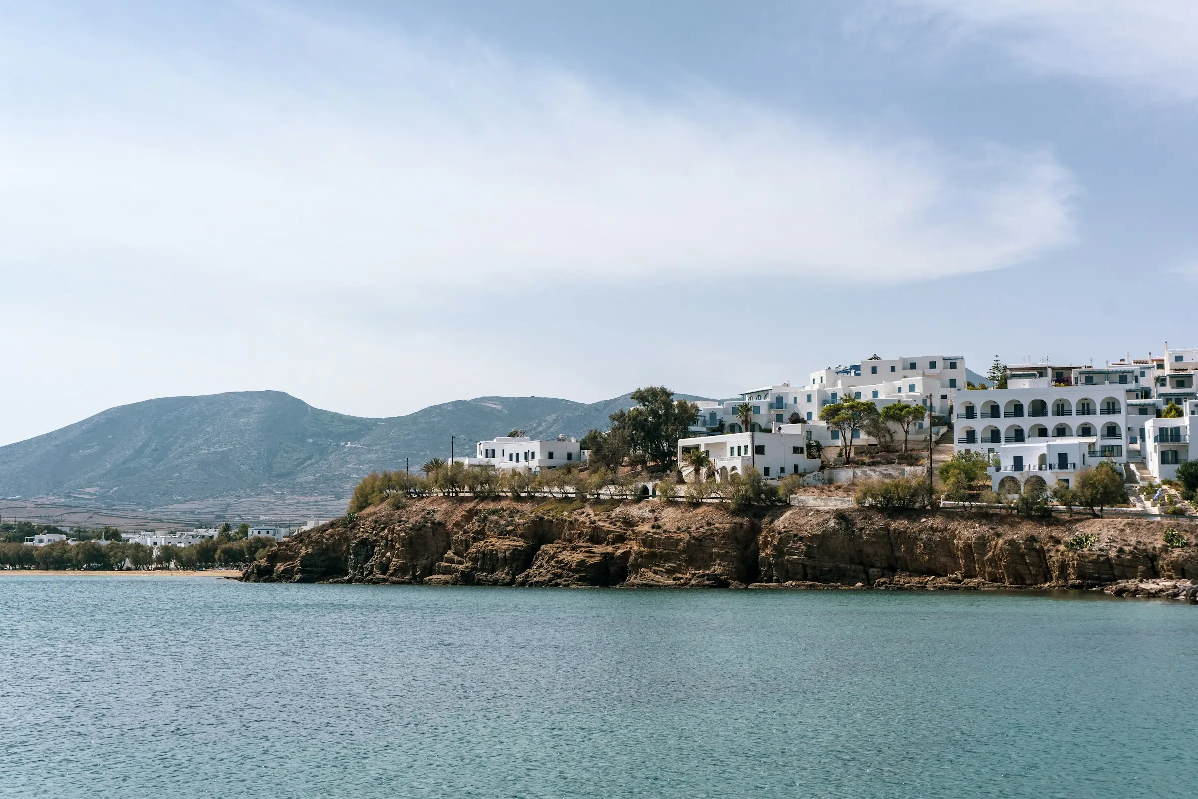 White buildings with arched balconies on a rocky headland above calm sea, Paros