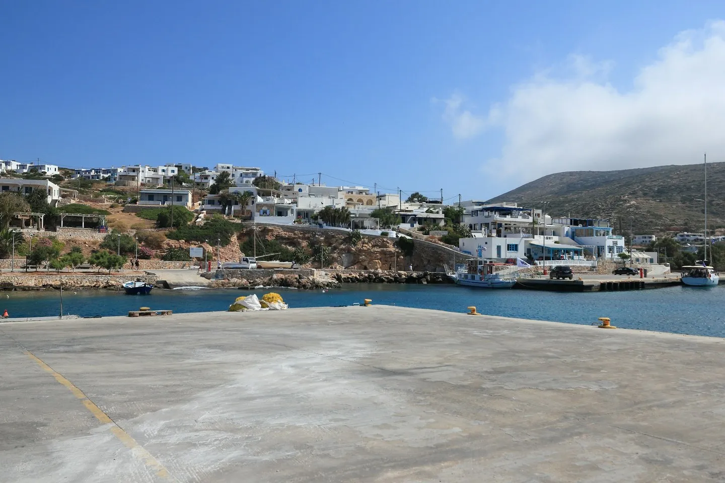 Donousa harbour with a concrete quay, moored boats and white houses on the hillside